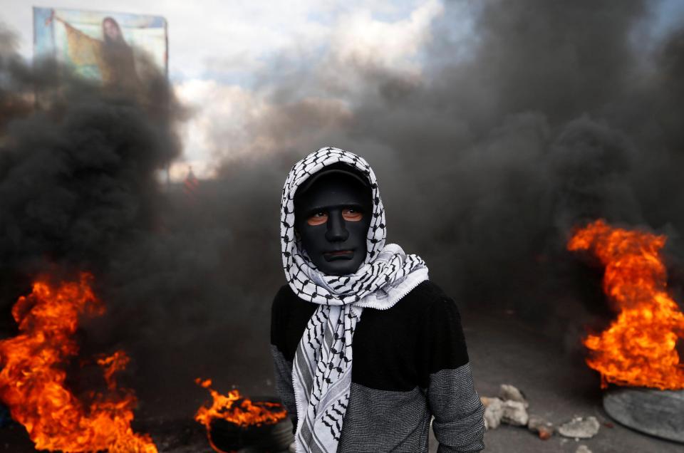 A masked demonstrator stands in front of burning tyres during clashes with Israeli troops 