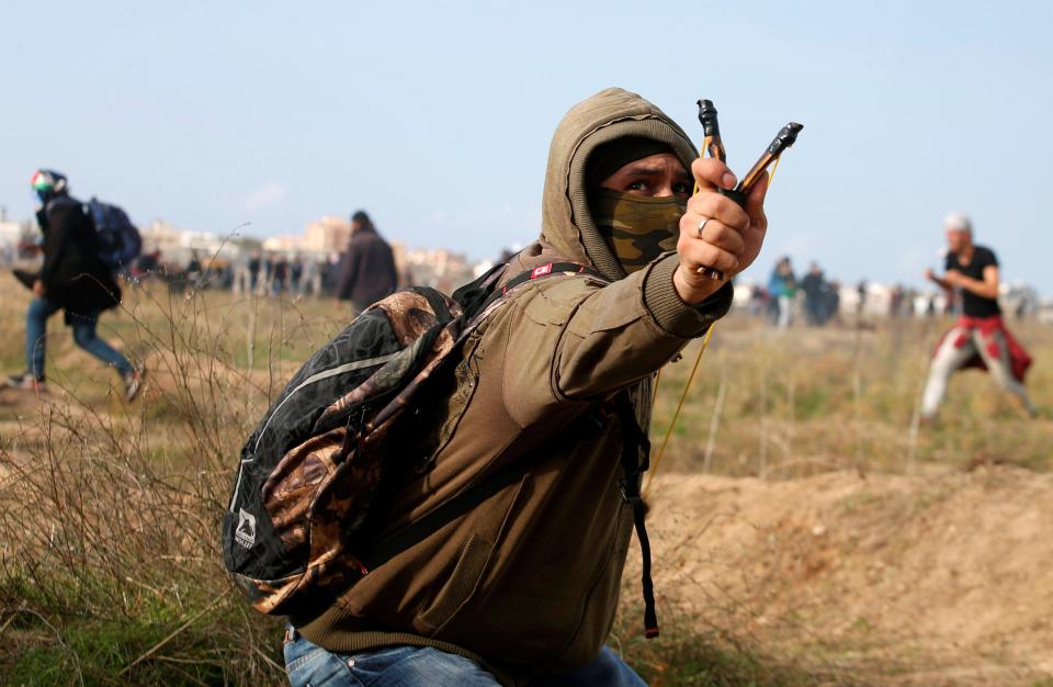 A Palestinian demonstrator fires rocks from a slingshot towards Israeli soldiers ear the border with Israel in the east of Gaza City