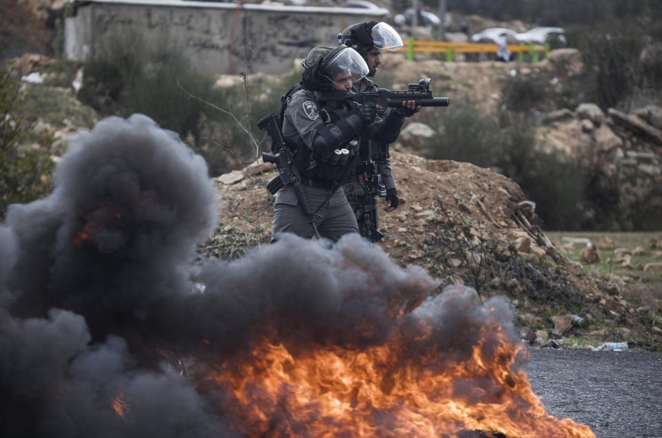 Israeli officers advance past burning tyres towards protesters hurling missiles in Ramallah, West Bank