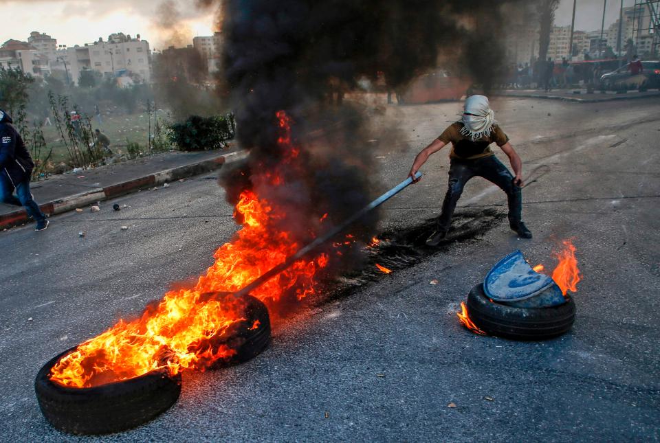 A Palestinian protester uses a stick to move flaming tyres during clashes with Israeli security forces