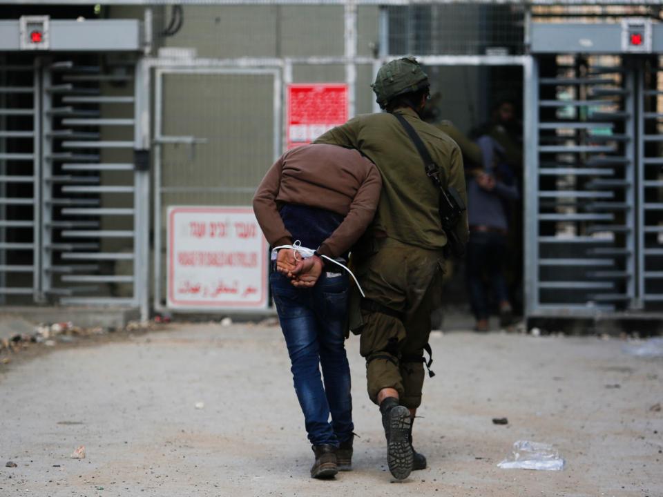 An Israeli soldier leads away a handcuffed Palestinian arrested at a protest in the West Bank city of Hebron