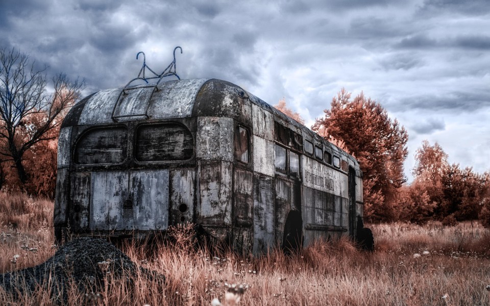 A charred bus decomposes against a sullen grey sky in Chernobyl