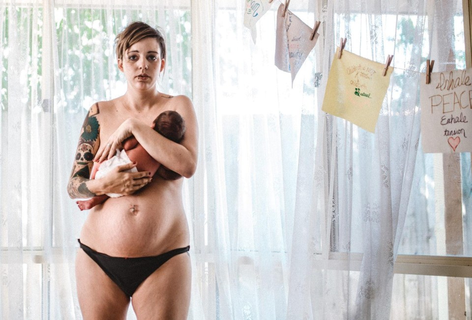 A tattoed mum stands holding her newborn baby 