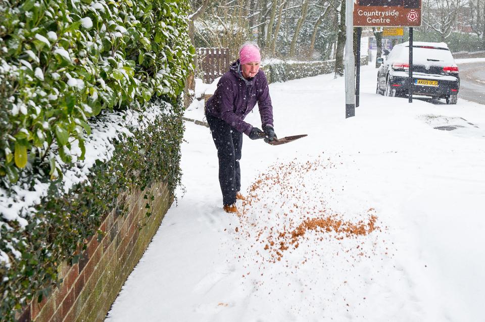  A woman grits the pavements near her home as heavy snow continues to fall in Saddleworth, Greater Manchester