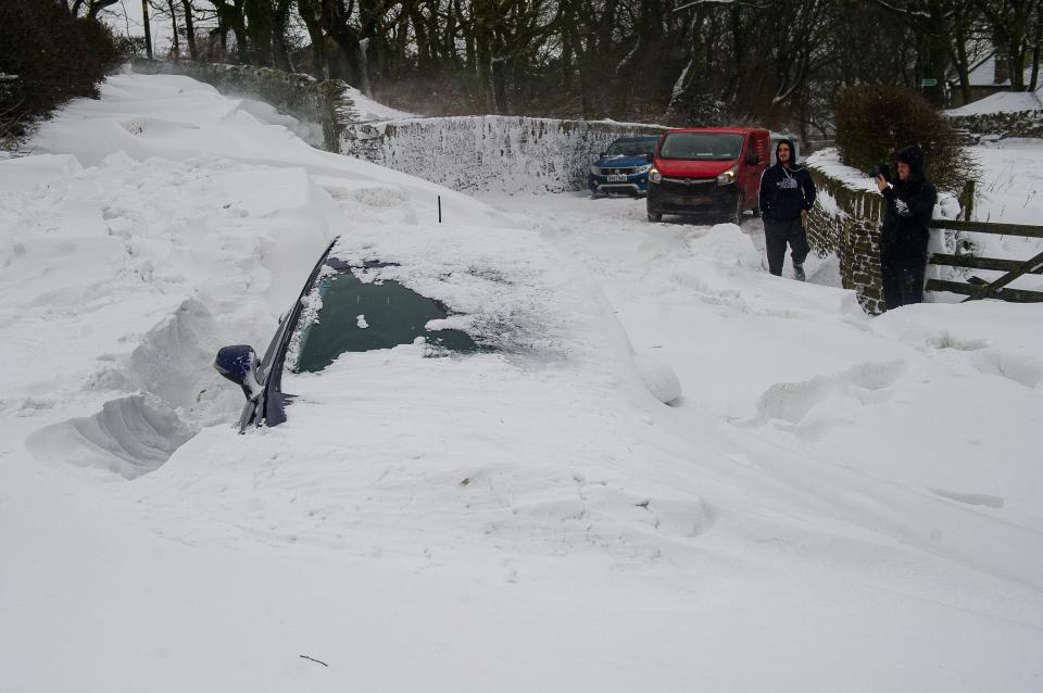  Motorists encounter an abandoned vehicle surrounded by several feet of snow in Saddleworth