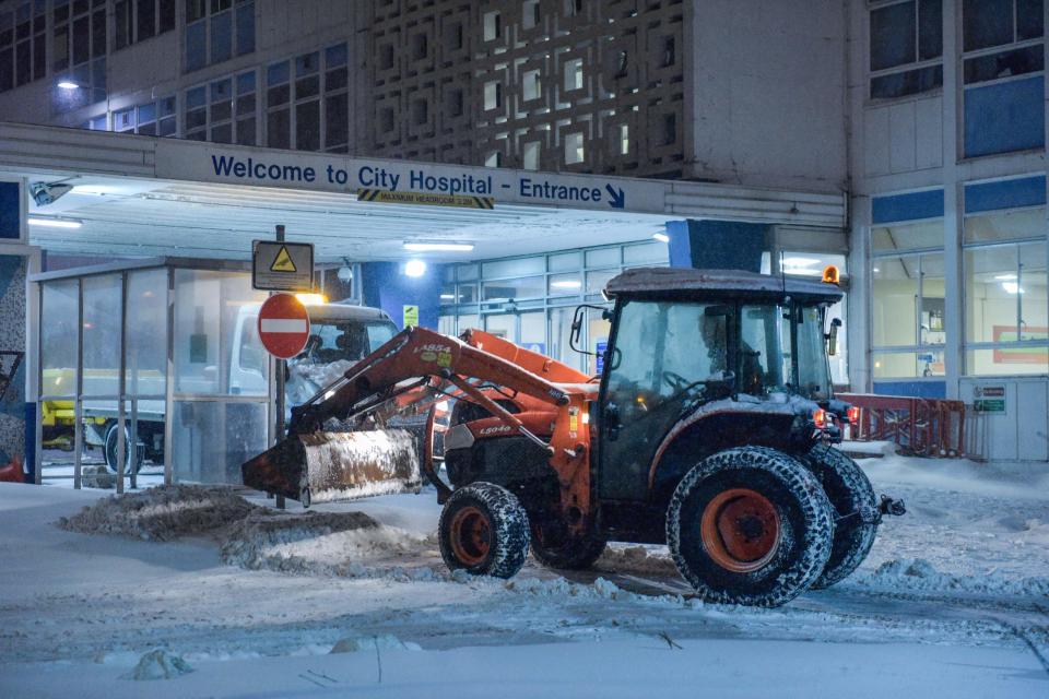  A worker battles the snow in a bid to clear an entrance to City Hospital in London