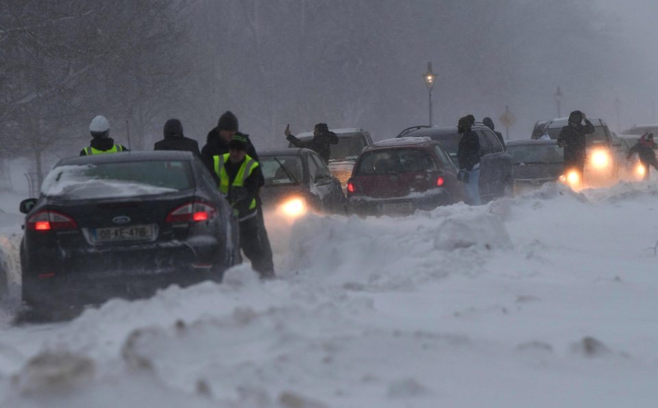  People try to push a car in a pile up of cars that have become stuck in heavy snow during a blizzard at night in Dublin