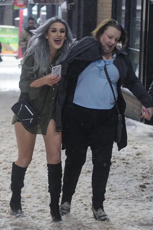 A woman wears knee high boots while helping her friend along a snow covered Broad Street in Birmingham city centre