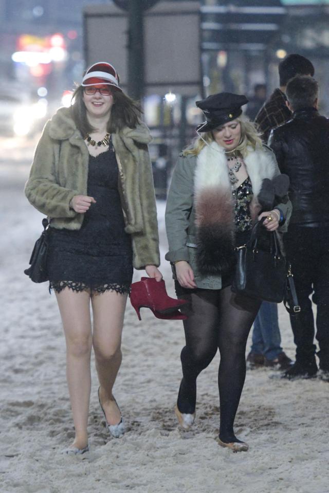 This woman on the left holds her high heels whilst she walks a snow covered Broad Street in Birmingham city centre in flats whilst wearing a short dress in the sub-zero temperatures