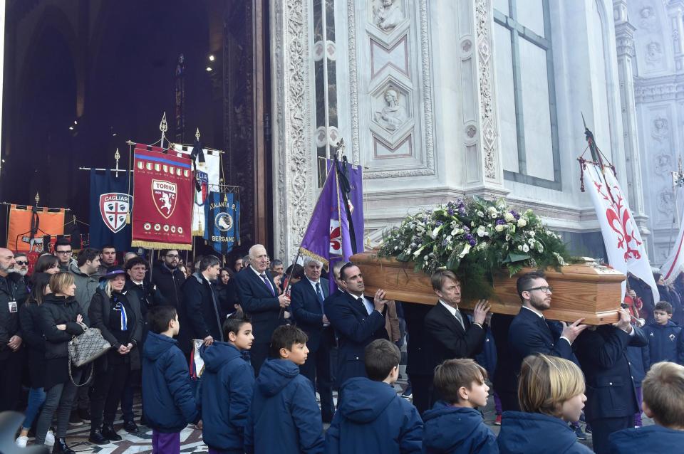 Astori's funeral coffin leaves the church followed by banners from AFC Fiorentina, followed by the crests of the Italian national team, Roma, Atalanta and Cagliari