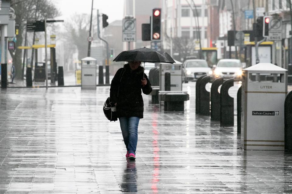  A woman with an umbrella walks through heavy rain in Southport, Merseyside