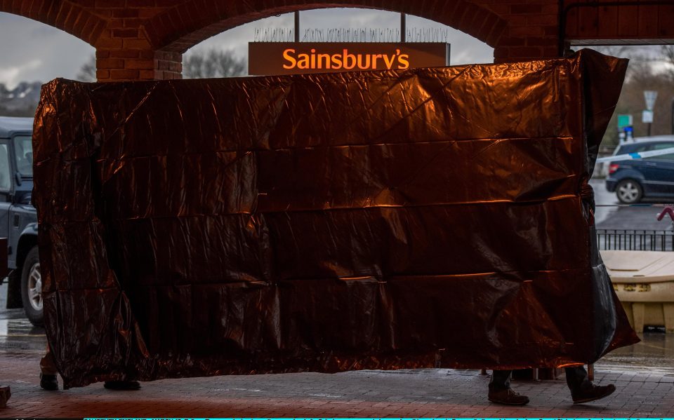  Police officers erect a barrier on the upper level of a Sainsbury's supermarket car park as it is cordoned off, opposite the park bench where Sergei Skripal was found