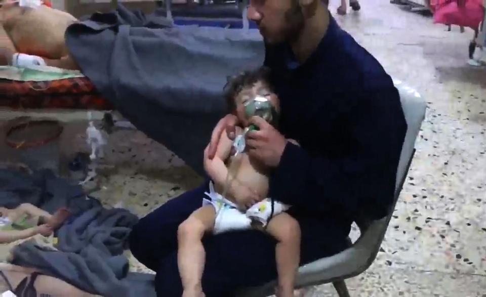  An unidentified volunteer holding an oxygen mask over a child's face in Douma