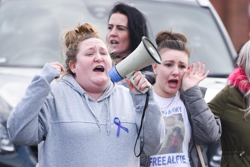  An visibly upset woman takes speaks on a megaphone while another appears to wipe a tear