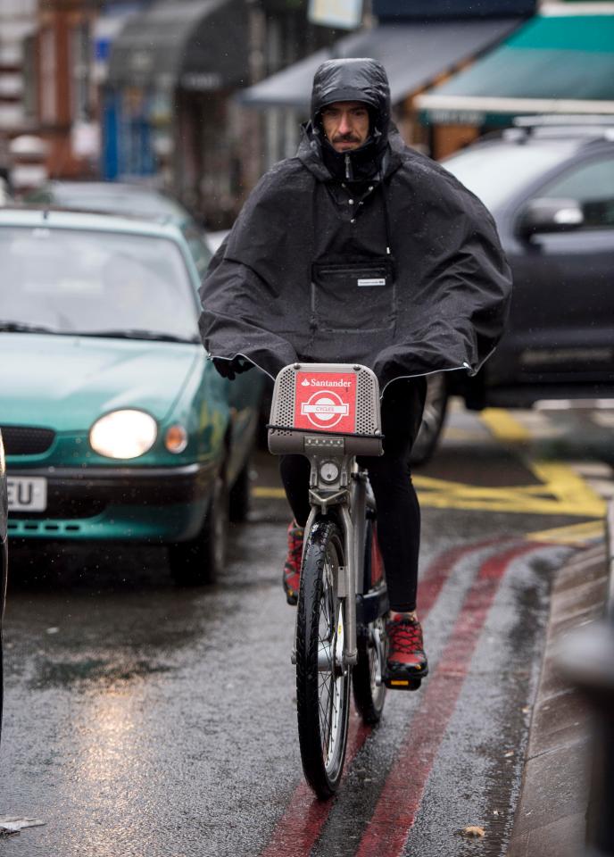  A man covers up to avoid the rain as he cycles through the wet on a Boris bike