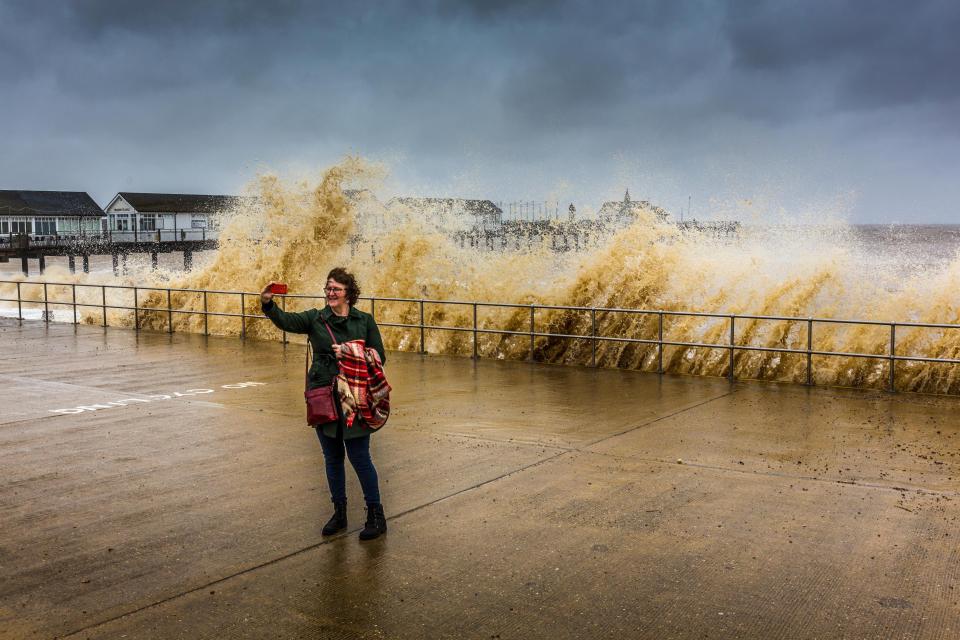  A lady takes a selfie in front of rough seas at Southwold pier, Southwold, Suffolk