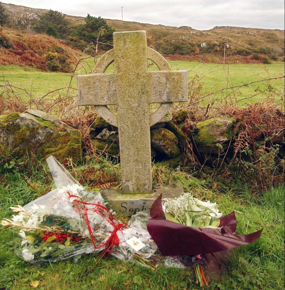  Floral tributes are left by the memorial cross, erected at the murder scene