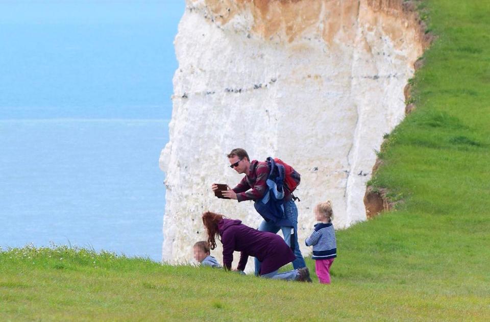  The young child appears to lie on his front as a woman holds him and a man takes their photo