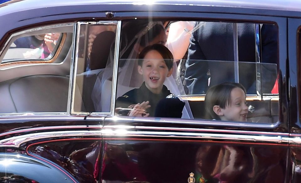  The cheeky pageboys flash a grin as they arrive with Meghan