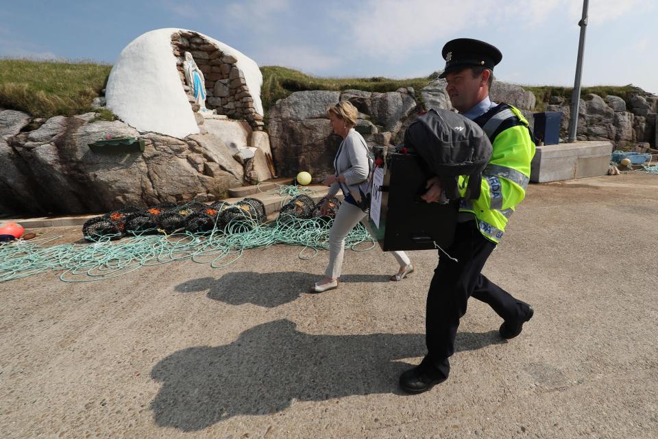  A police officer carries one of the ballot boxes past a shrine to the Virgin Mary