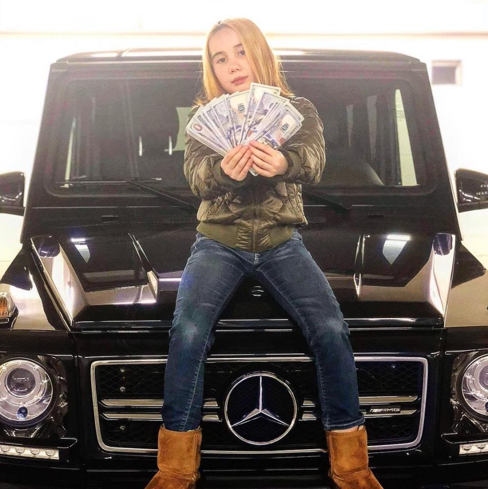  Lil Tay poses with a fistful of cash on top of a car she claims belongs to her