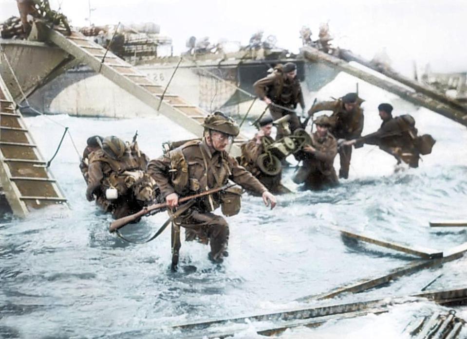  Royal Marines descend from landing craft with their heavy backpacks, weapons and equipment on Juno beach