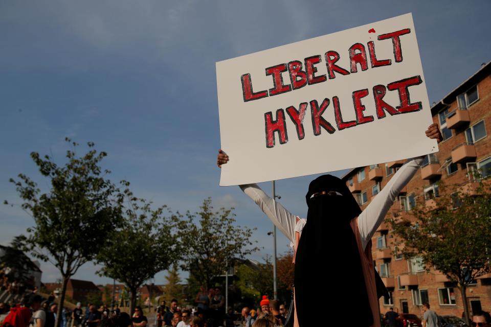  A veiled woman holds a banner translating as "Liberal Hypocrisy"