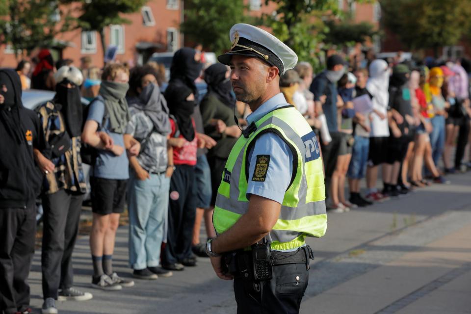  A police officer watches as masked protesters surround Bellahoj police station