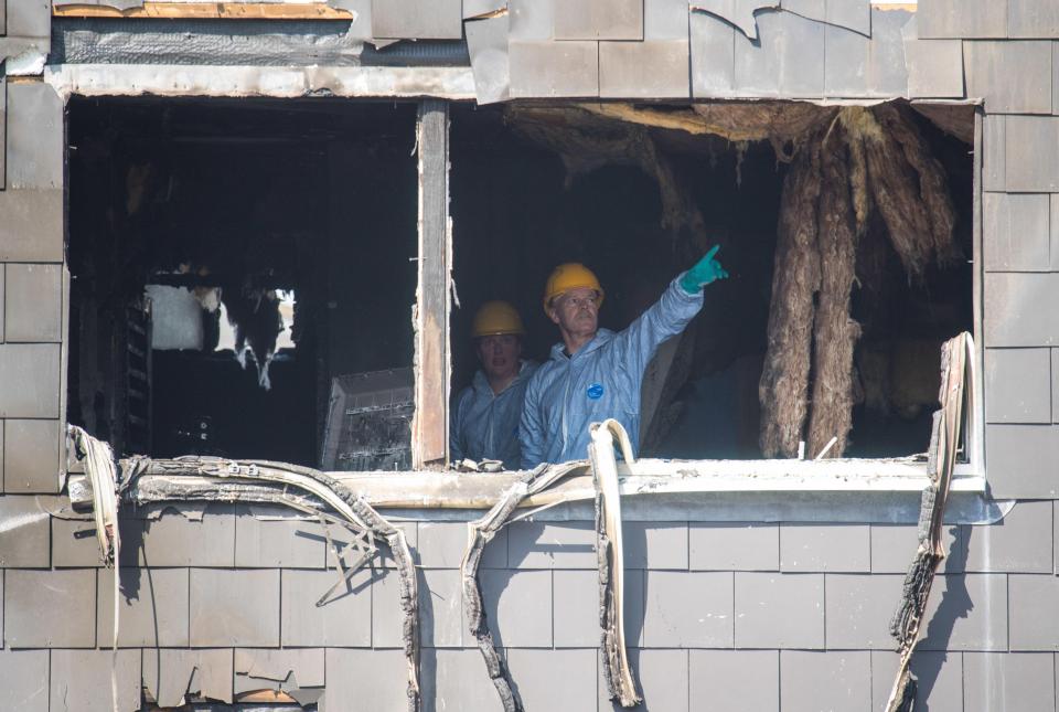 Forensic officers can be seen looking at points of interest as they examine the burned house