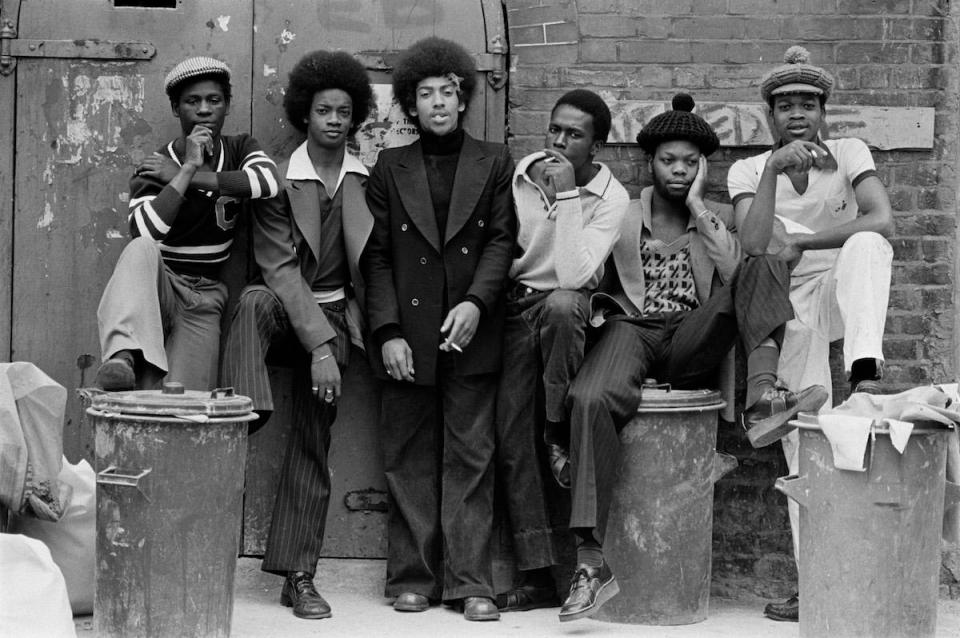  Colin Jones captures a group posing while smoking and looking bored, some leaning on trash cans. The photo Untitled, appears in the series The Black House, 1973-1976. Colin spent his childhood in working class East London while dancing for the English National Ballet