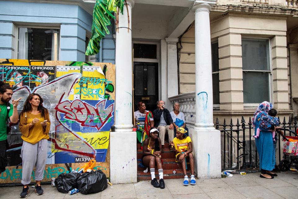  Revellers take a perch on a door step of a house which has boarded up its windows