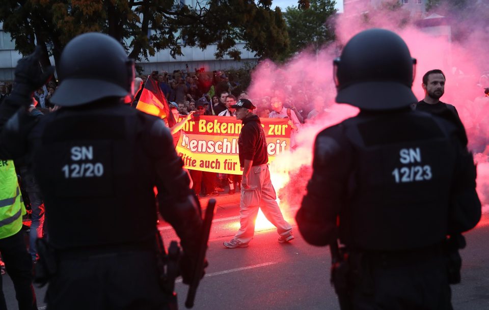  Two riot officers watch on as a demonstrator carries a flare through the streets