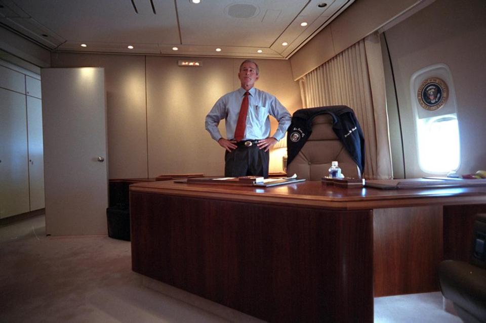  The President standing behind his desk on Air Force One watches TV as he flies to Louisiana