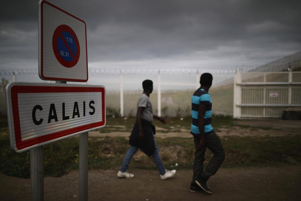  Migrants walk past security fencing in the 'Jungle'