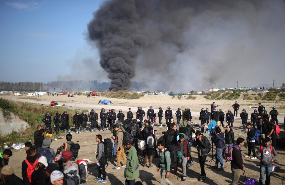  Police officers stand outside the notorious Jungle camp as migrants prepare to leave in October 2016