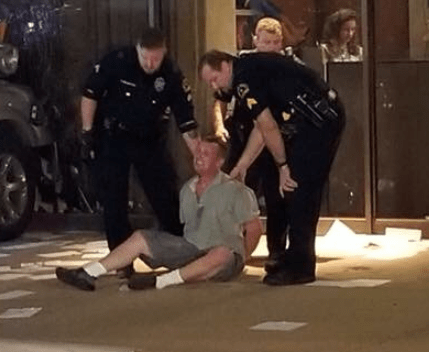  A man sits on the ground as police officers swarm around him