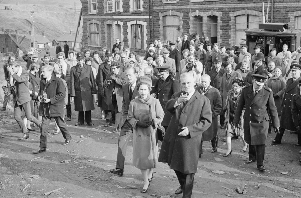  The Queen is flanked by policemen and mourning villagers during the visit in 1966