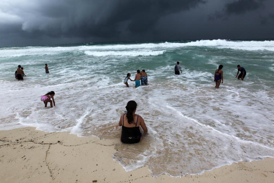  Swimmers in the turbulent sea at a beach in Cancun, Mexico, as storm clouds loom overhead