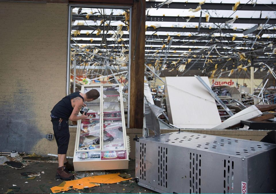  A man takes some cigarettes from a cabinet at a destroyed corner store