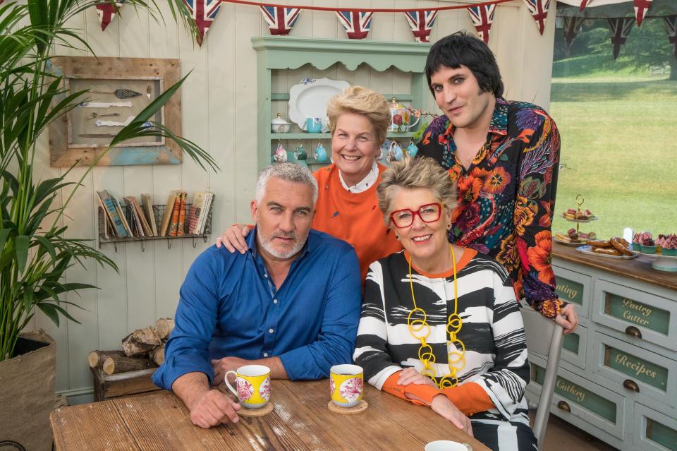  Judges Paul Hollywood and Prue Leith sitting with Bake Off presenters Sandi Toksvig and Noel Fielding standing inside the famous white tent