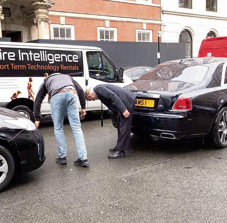 Sir Alan Sugar's chauffeur inspects the damage after he reversed into an Uber while trying to park 