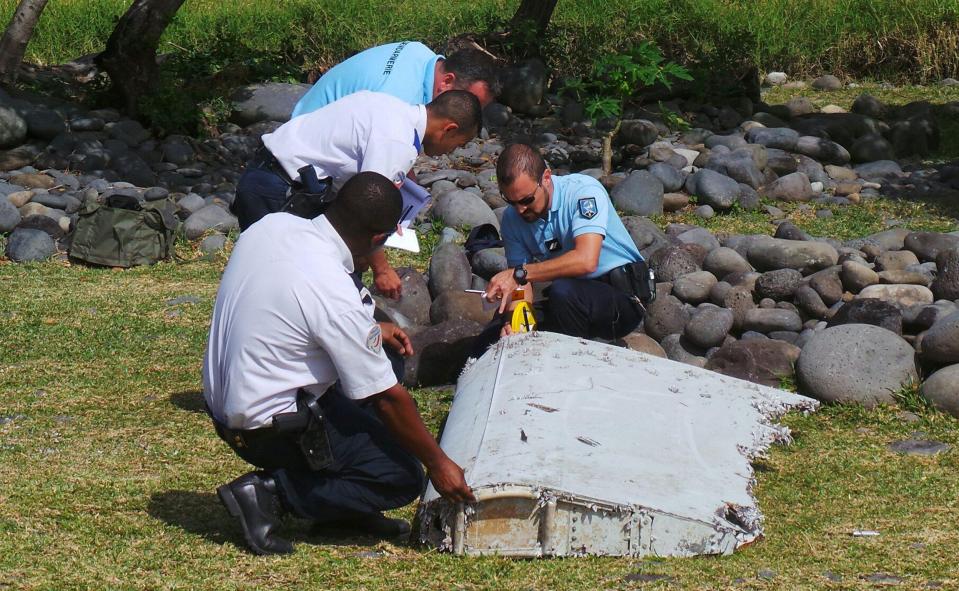 French gendarmes and police inspect a large piece of plane debris which was found on the beach in Saint-Andre, on the French Indian Ocean island of La Reunion in 2015