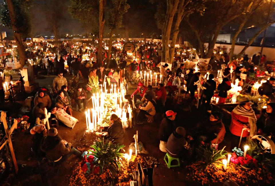 People stand next to graves on the Day of the Dead to pay homage to their dead relatives at the cemetery of Metepec on the outskirts of Mexico City