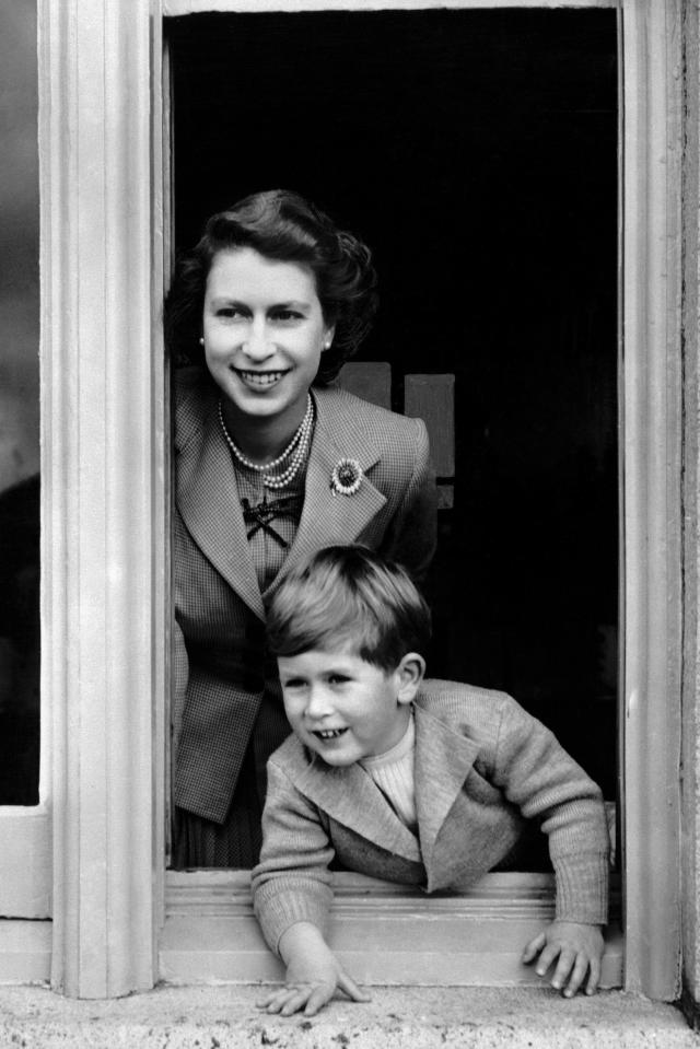  1952: Prince Charles keeping a look out on his fourth birthday, as he leans from a window with his mother