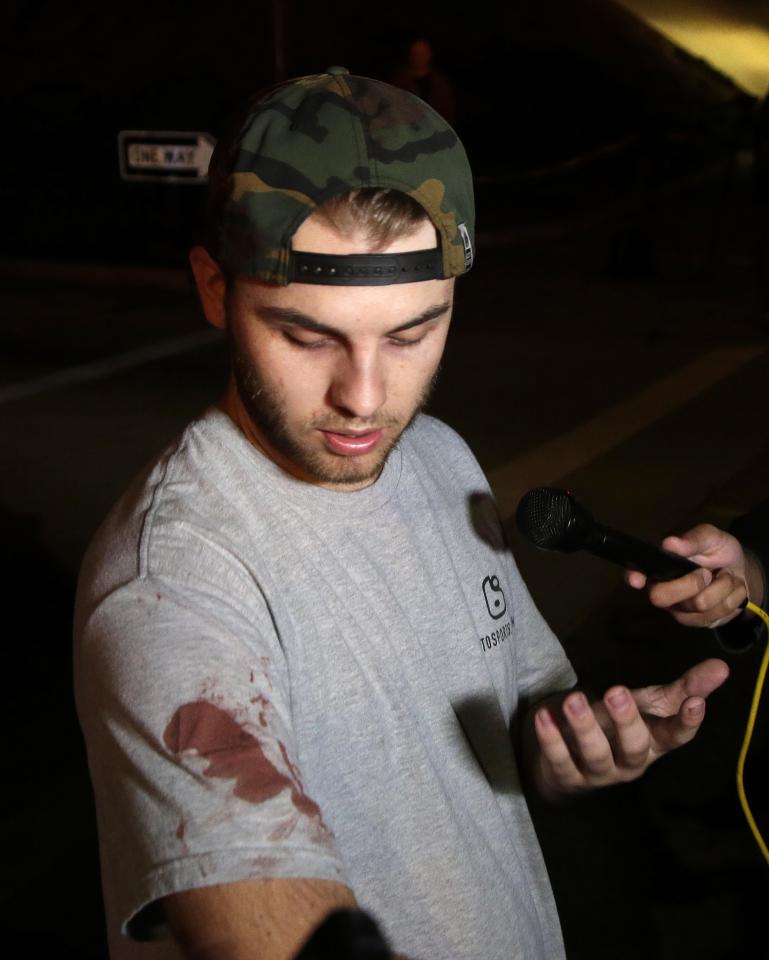  A young man with blood on his t-shirt talks to reporters following the massacre