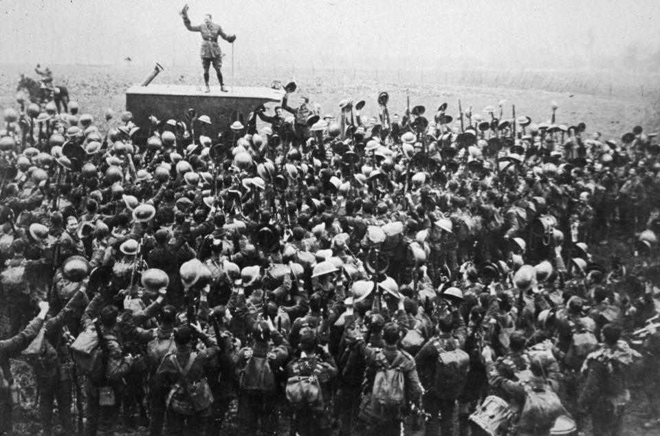 A crowd of soldiers on the Western Front celebrating as an officer announces the news of the armistice on Nov 11, 1918