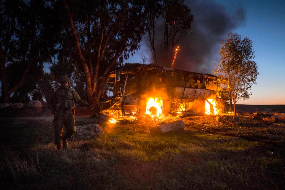  An Israeli soldier stands near a burning bus after it was hit by a mortar shell fired from Gaza near the Israel Gaza border