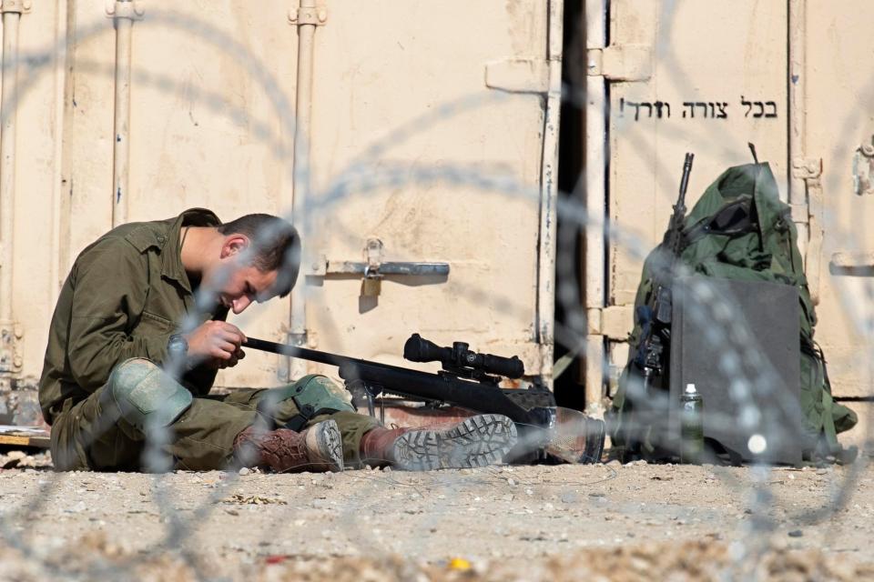  An Israeli soldier cleans his high power rifle complete with a scoop on a small Israeli army base along the border with the Gaza Strip