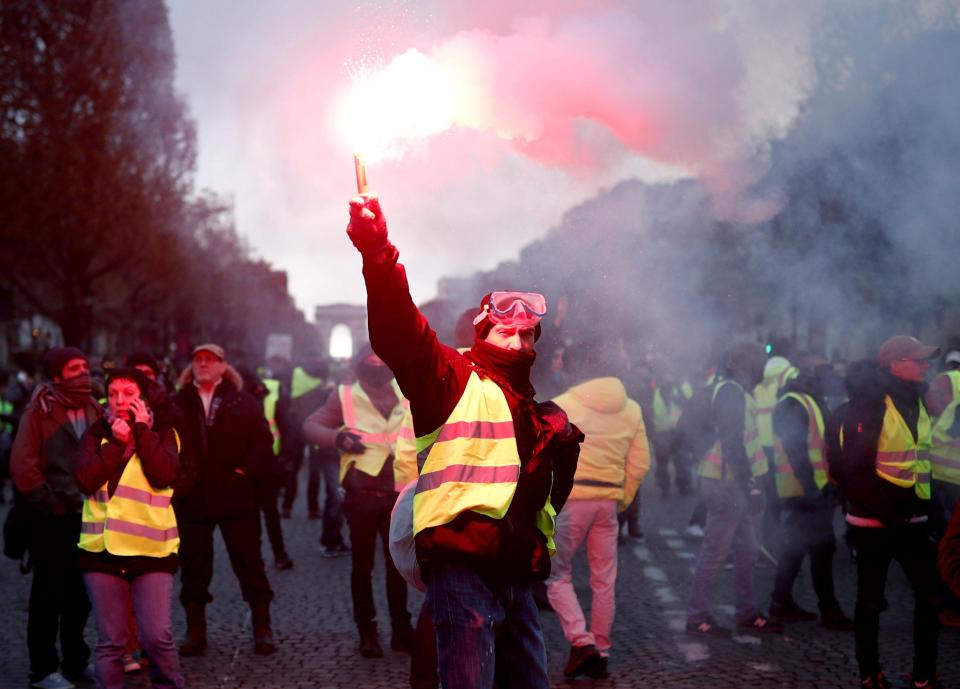  A protester wearing yellow vest, a symbol of a French drivers' protest against higher fuel prices, burns flare on the the Champs-Elysee