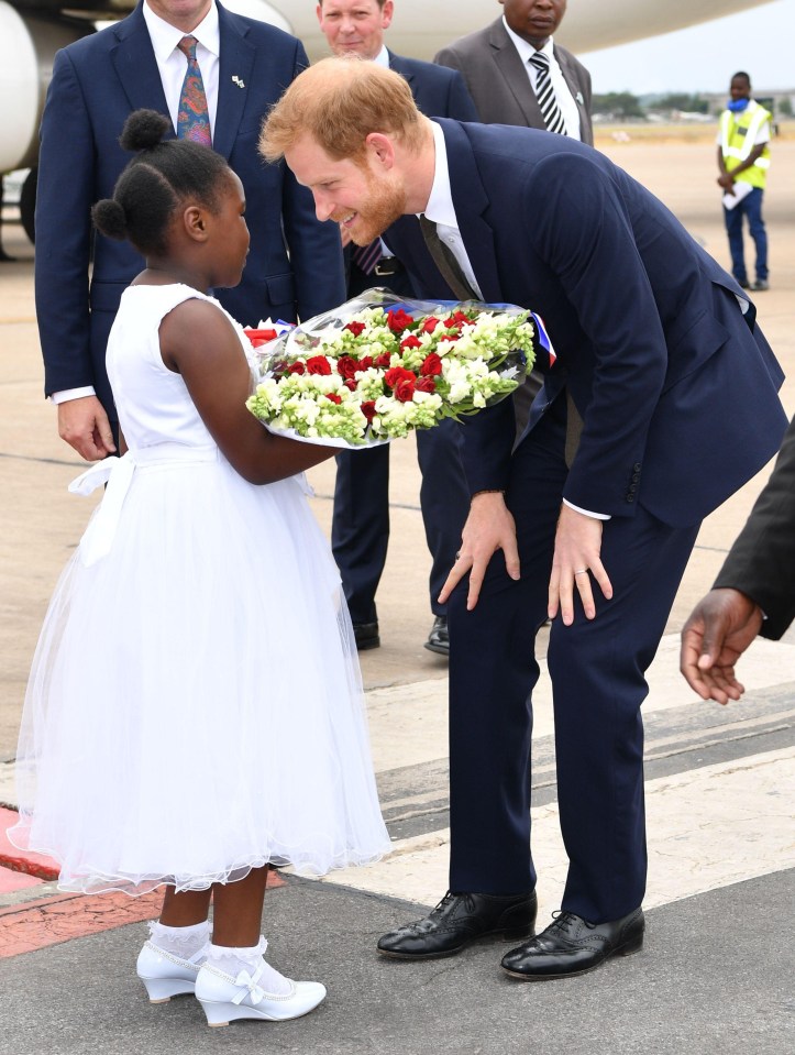 A young girl offers Prince Harry a bouquet of flowers upon his arrival in Zambia